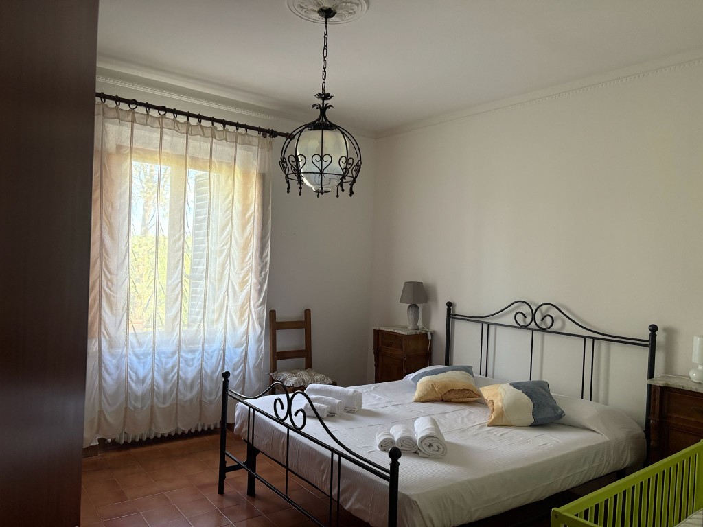 Camera matrimoniale con lampadario ornato e vista giardino a Villa Talciona, Toscana