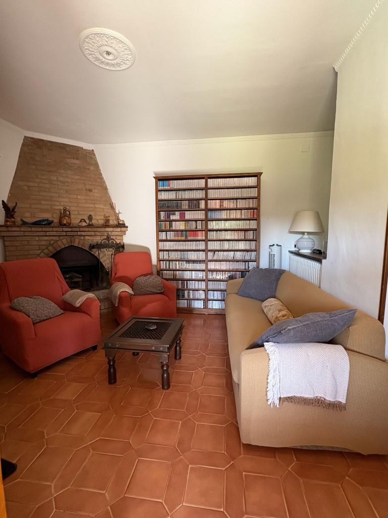 Soggiorno con camino in mattoni, poltrone rosse e libreria a Villa Talciona
